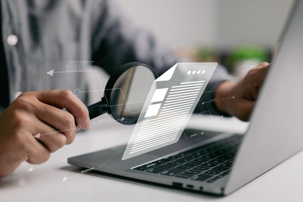 Man looking at laptop data with a magnifying glass